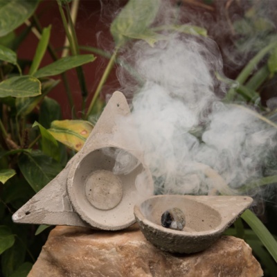 Incensário de cerâmica cinzenta triangular e redondo com fumo branco sobre pedra