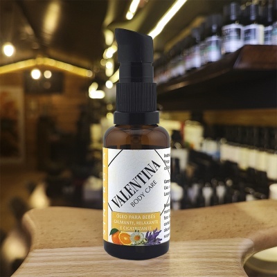 Frasco âmbar com óleo corporal para bebés VALENTINA com doseador preto sobre superfície de madeira