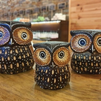 Três coadores de café cerâmicos em forma de coruja com olhos coloridos, sobre mesa de madeira