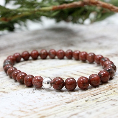 Pulseira elástica de contas vermelhas e uma conta prateada sobre madeira clara