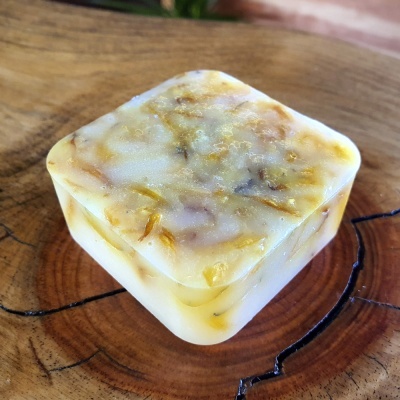 Sabonete artesanal quadrado branco translúcido com inclusões amarelas e castanhas sobre madeira