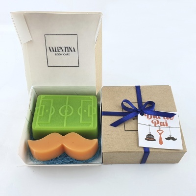 Sabonetes em caixa com campo de futebol e bigode, embalagem kraft com laço azul e etiqueta 