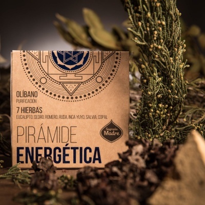 Embalagem de papel castanho com texto preto do produto Pirámide Energética rodeada por plantas e folhas secas