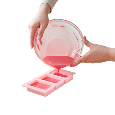 Mãos despejando mistura rosa de tigela para forma de silicone rosa com três compartimentos