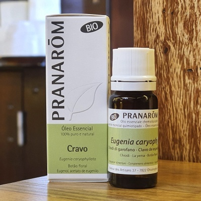 Frasco e caixa de óleo essencial de Cravo da marca Pranarôm sobre superfície de madeira.