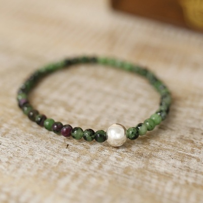 Pulseira de contas verdes e roxas com pérola central sobre madeira clara