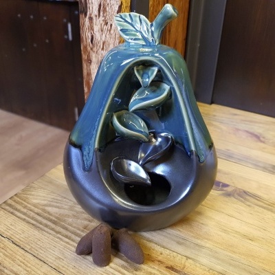 Escultura de pêra em cerâmica vidrada azul e preta numa mesa de madeira.