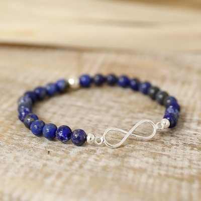 Pulseira de contas azuis com fecho infinito prateado sobre madeira clara.