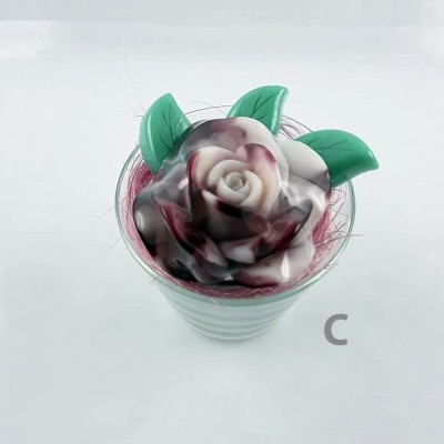 Vaso pequeno branco com flor decorativa de rosa e folhas verdes.