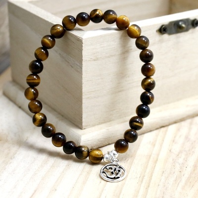 Pulseira de contas olho de tigre com pendente Om, sobre superfície de madeira e caixa de madeira.