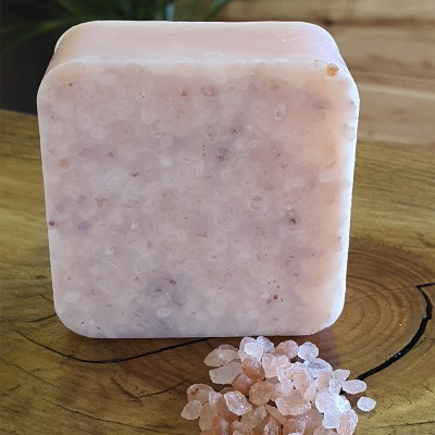 Sabonete quadrado cor de rosa claro com textura rugosa e grãos de sal rosa numa superfície de madeira