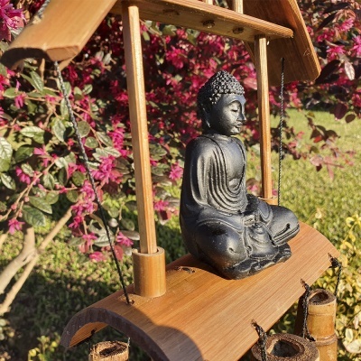 Estátua preta de Buda sentado em suporte de madeira pendente na natureza