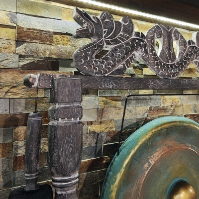 Gong metálico com suporte de madeira entalhada numa parede de pedra