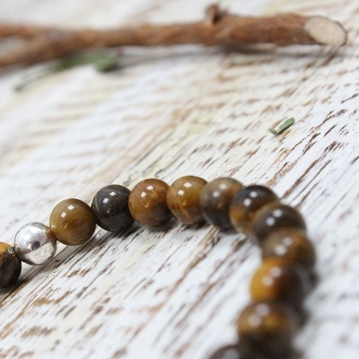 Pulseira de contas castanhas e metálica sobre madeira clara