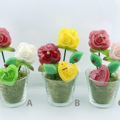 Três vasos com flores artificiais em cera e corações decorativos, etiquetados como A, B e C