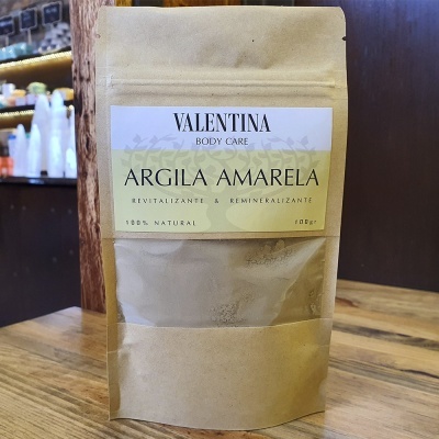 Embalagem de argila amarela Valentina Body Care em saco de papel castanho sobre mesa de madeira