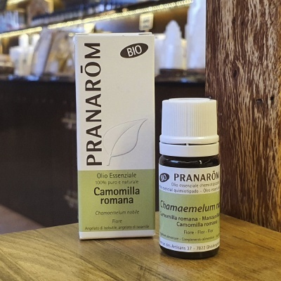 Frasco de óleo essencial Pranarôm Camomilla romana com caixa branca e verde sobre madeira