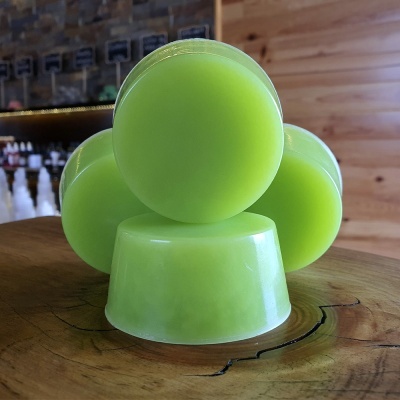 Quatro sabonetes verdes empilhados sobre madeira polida com fundo de prateleiras e parede de madeira.