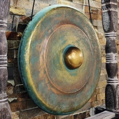 Escudo redondo metálico envelhecido em verde e dourado numa parede de pedra.