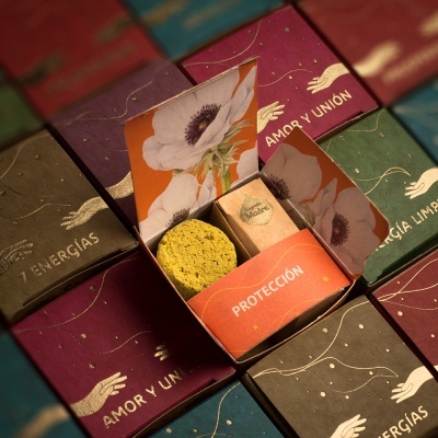 Caixas coloridas com ilustrações florais e texto em espanhol, uma caixa aberta mostrando sabonete ou esponja amarela