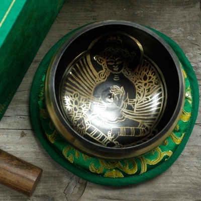 Tigela de meditação preta com decoração dourada sobre almofada verde e bastão de madeira