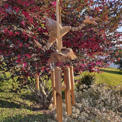 Sino dos ventos de madeira e cortiça suspenso numa árvore com folhas vermelhas e verdes