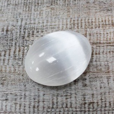 Pedra polida oval branca sobre superfície de madeira rústica.