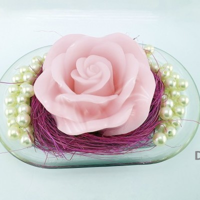 Vela rosa em forma de rosa sobre base transparente com pérolas brancas e fios roxos