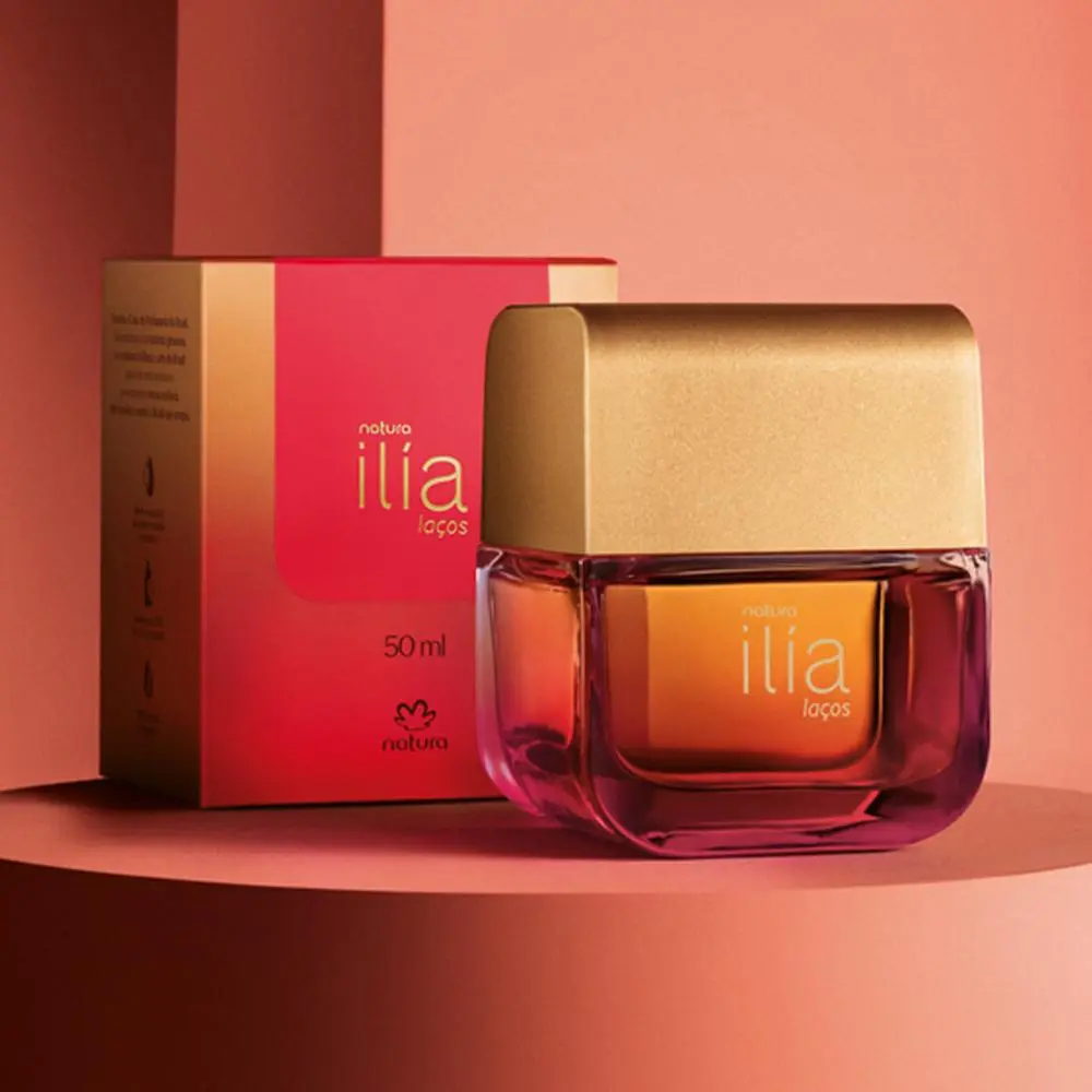 Frasco de perfume Natura Ilía Laços 50 ml com embalagem vermelha e dourada em fundo rosa