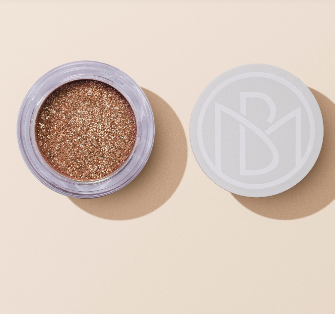 Pote aberto de sombra de olhos dourada com tampa branca ao lado