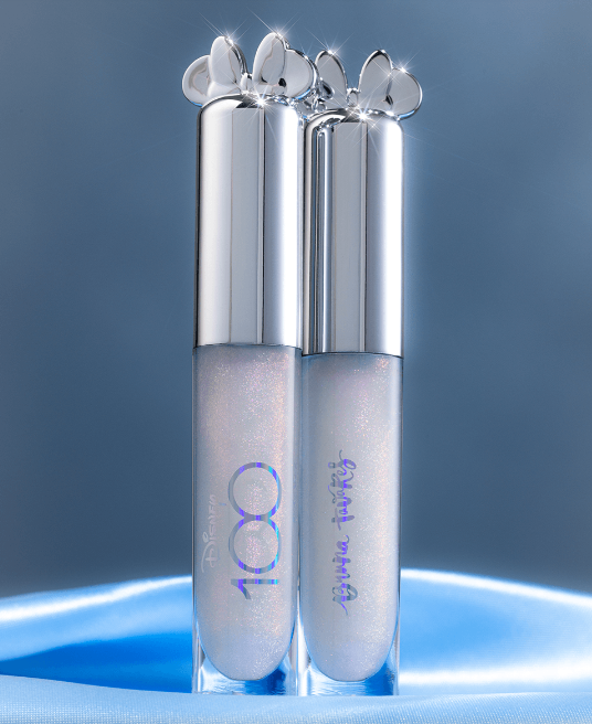 Duas embalagens de gloss de lábios com tampa prateada e detalhes de corações sobre fundo azul.