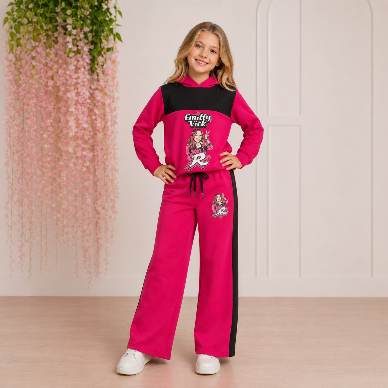 Conjunto rosa e preto para criança com estampa Emilly Vick e letra R, em interior com planta pendente e parede branca