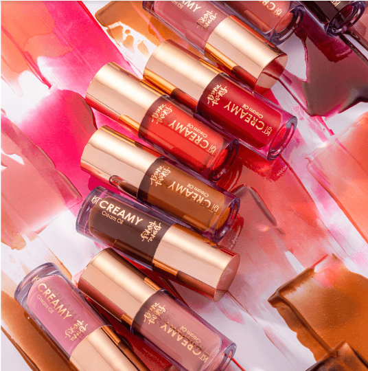 Batons líquidos em várias cores com tampas douradas sobre fundo colorido com amostras de batom.