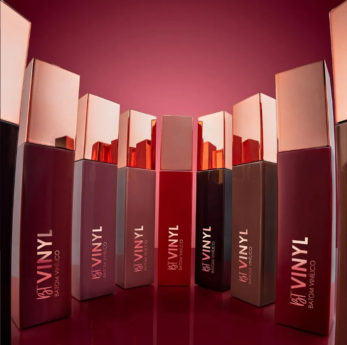 Vários batons líquidos em tons vinho e vermelho com tampa dourada, sobre fundo vermelho.