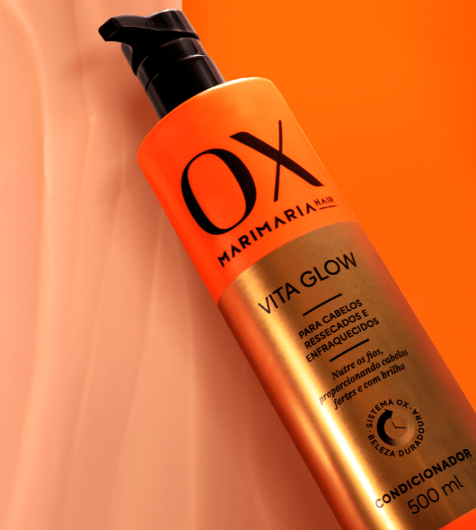 Frasco laranja e dourado de condicionador OX Marimaria Hair sobre fundo laranja e creme