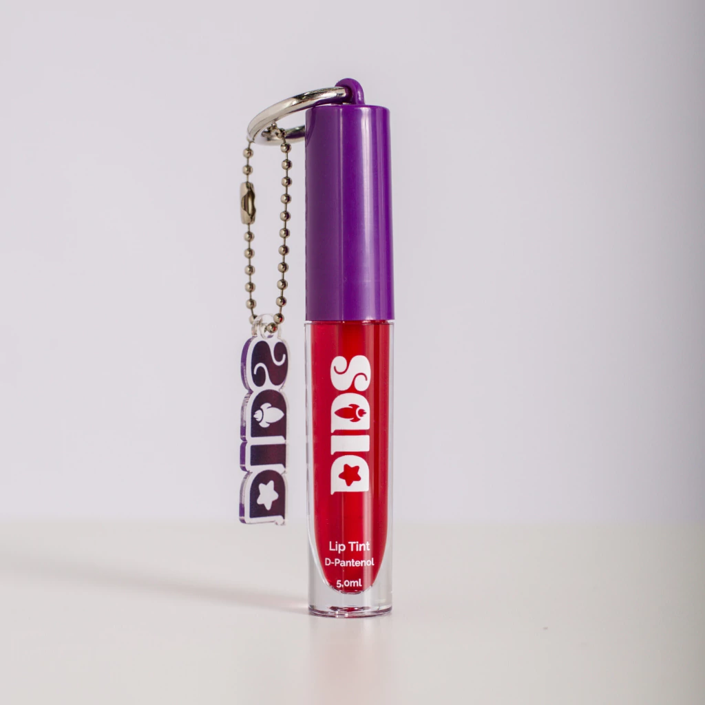 Lip Tint em embalagem transparente com tampa roxa e líquido vermelho, pendente roxo com chave metálica