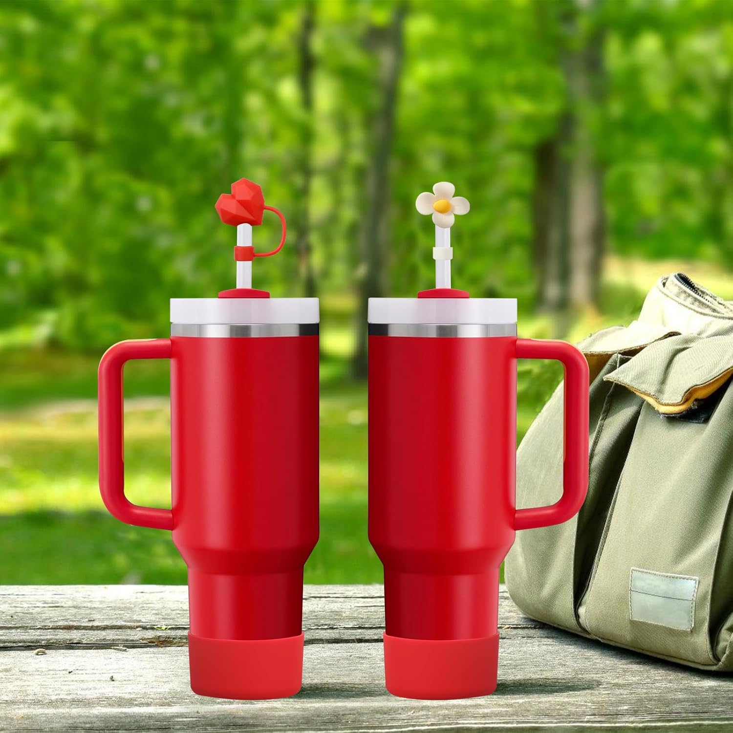 Dois copos térmicos vermelhos com canudos decorados e mochila ao lado sobre mesa em ambiente exterior