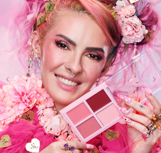 Paleta de maquilhagem com cinco tons em caixa rosa segurada por mulher com cabelo rosa e acessórios florais