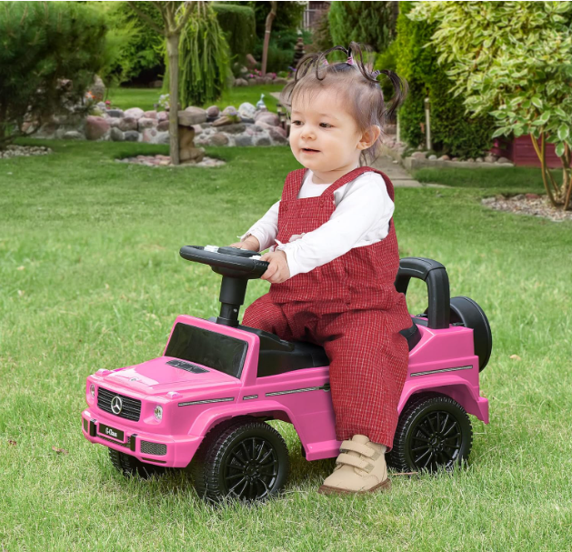 Criança num carro elétrico de brincar cor-de-rosa Mercedes no jardim