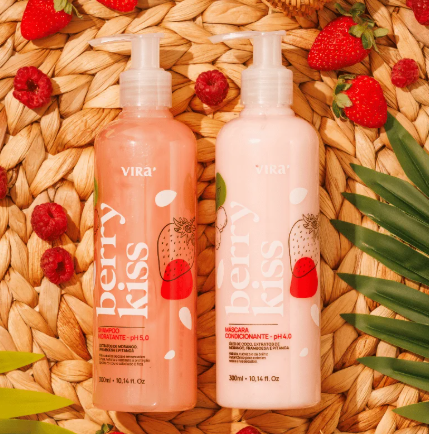 Duas garrafas rosas e bege com rótulo berry kiss da marca VIRA, rodeadas de morangos e framboesas sobre uma superfície de palha.