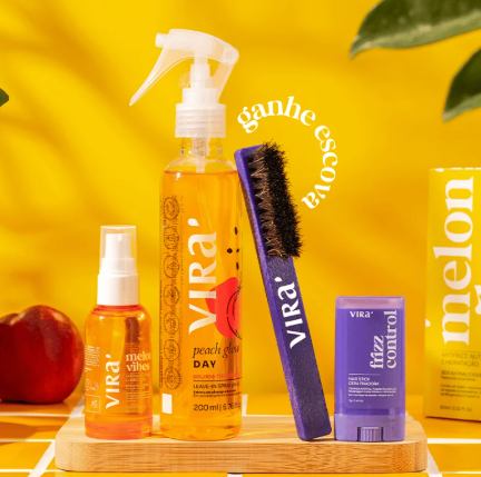 Produtos para cabelo da marca VIRA em frascos laranja e violeta sobre base de madeira com fundo amarelo