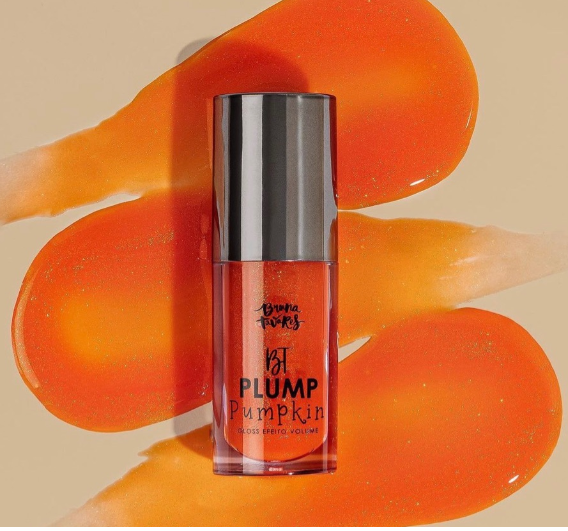 Frasco pequeno de gloss labial laranja com tampa preta sobre manchas alaranjadas.