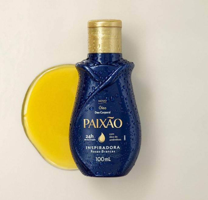 Frasco azul escuro com tampa dourada de óleo corporal PAIXÃO com óleo amarelo ao lado