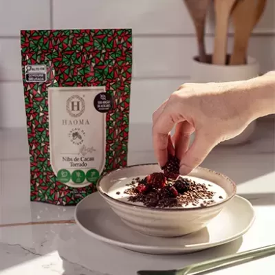 Embalagem de nibs de cacau torrado ao lado de tigela com iogurte e frutas