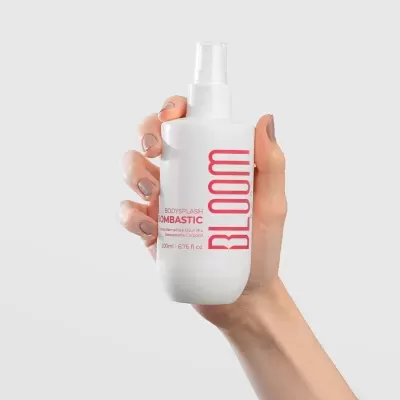 Frasco branco de bodysplash com texto vermelho BLOOM em mão feminina