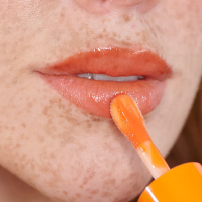 Lábios com brilho labial laranja aplicado com aplicador.