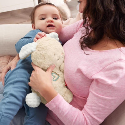Bebé com macacão azul e mulher com camisola rosa segurando brinquedo de peluche creme