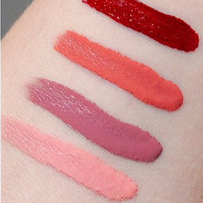 Quatro amostras de maquilhagem líquida em tons rosa, vermelho e coral sobre pele.