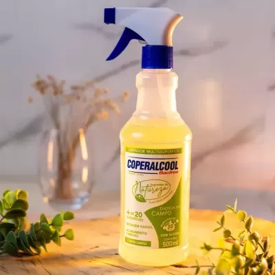 Frasco de spray de produto de limpeza amarelo com rótulo verde e azul sobre mesa de madeira com plantas ao redor