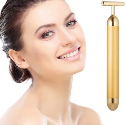 Mulher sorridente com massageador facial dourado em fundo branco